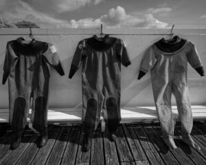 Three wetsuits hanging to dry on a line, captured in black and white.