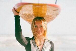 Smiling young woman holding a surfboard on the beach, capturing a carefree summer vibe.