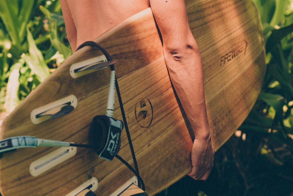 Close-up of a surfer holding a wooden surfboard amidst lush tropical greenery, perfect for summer vibes.